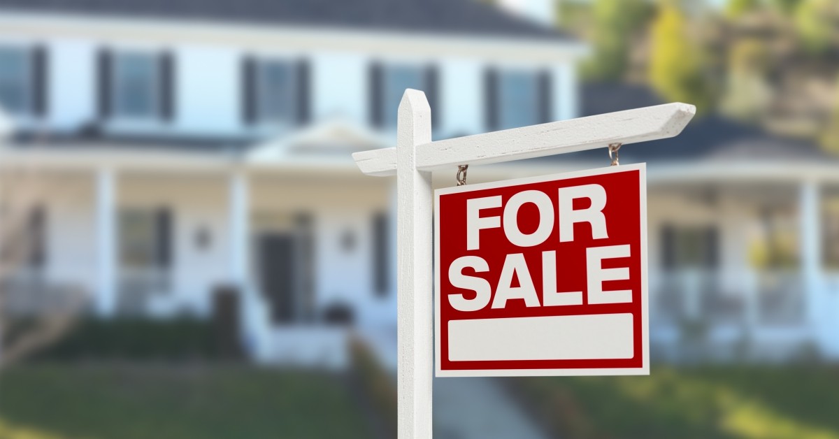 Red and white For Sale sign in front of white and gray two-story home