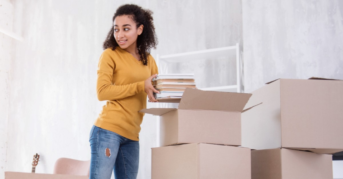 Woman in yellow shirt and blue jeans packing boxes into moving box