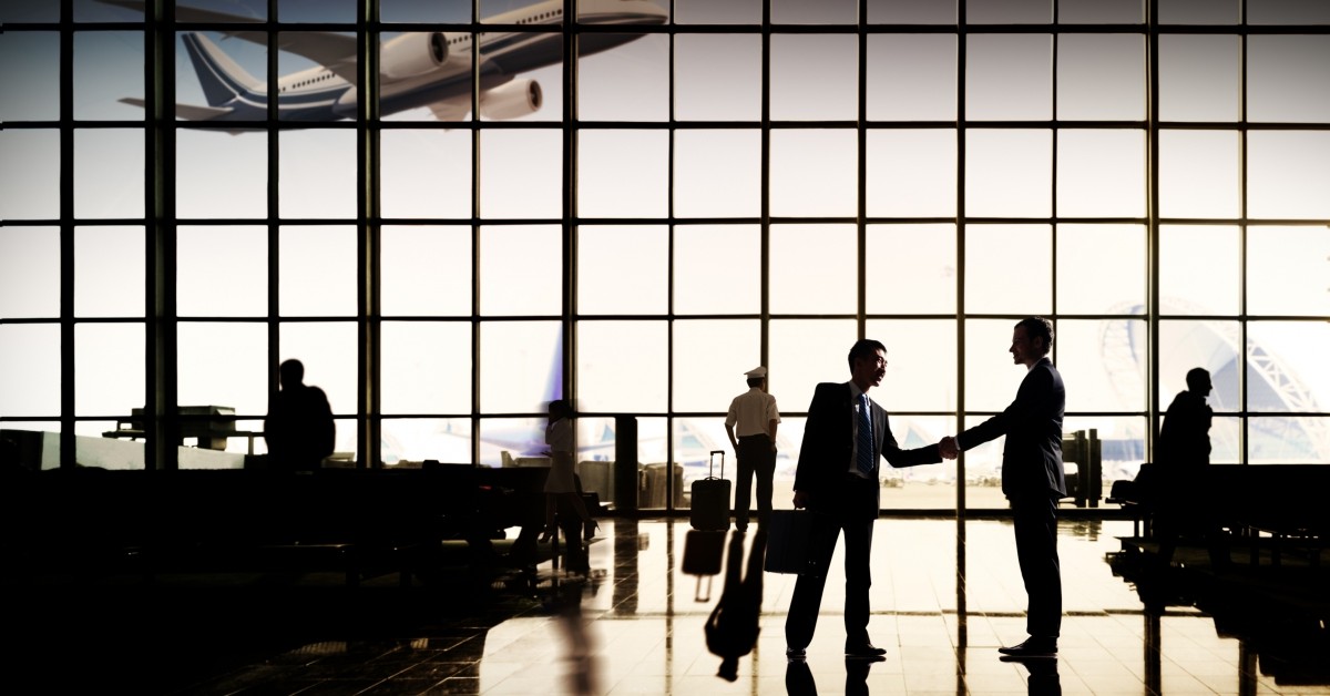 Airport with multiple people, two men shaking hands in foreground