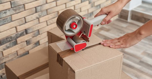 Close-up of hands using packing tape to seal a cardboard box