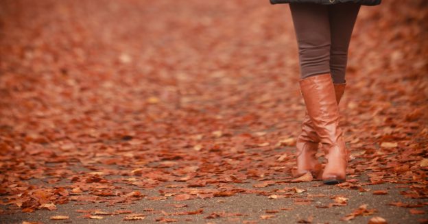 Close up of a woman's feet, wearing leather boots, standing in a road with fallen leaves