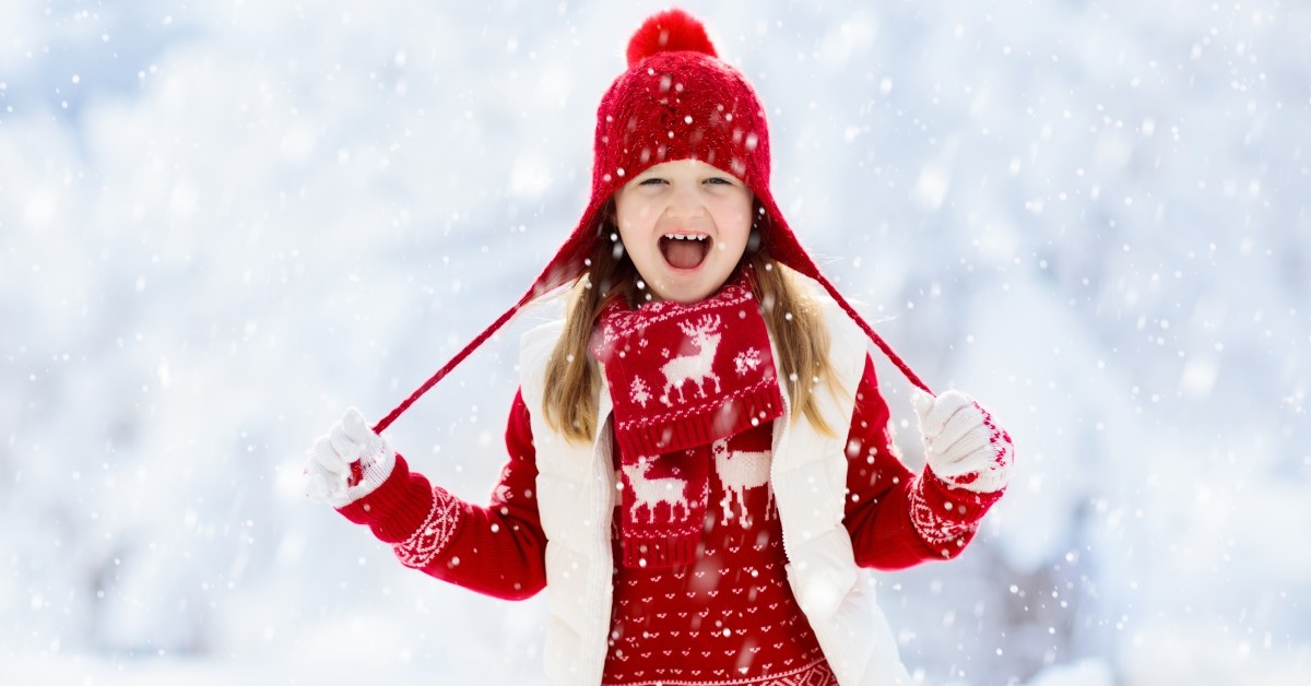 Laughing girl playing in the snow wearing red holiday-pattern sweater and hat