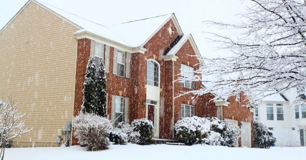 Frontal/side view of residential two-story brick home during a heavy snow.