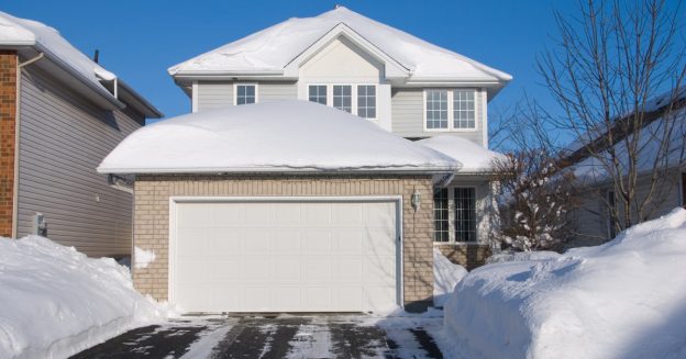 Rear view of residential home and garage with snow on the roof