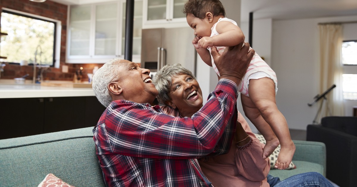 Grandparents sitting on couch smiling and holding a baby with kitchen in background