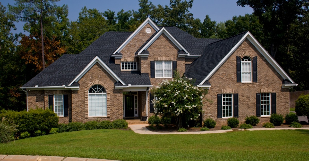 Front view of a two-story residential home with gables, manicured green lawn and driveway.