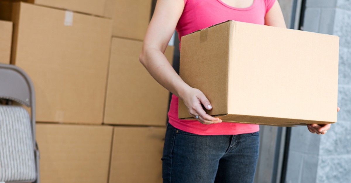 Close up of woman holding a brown moving box while standing in doorway of storage unit.