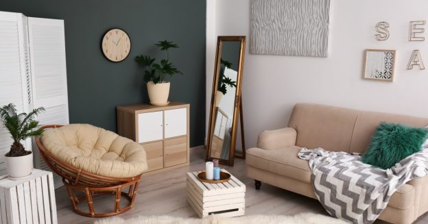 Scene of an apartment living room with sofa, chair, mirror and wall decor.