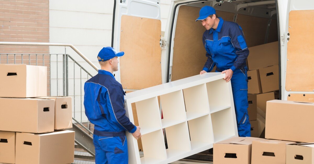 Two smiling professional movers unloading a van with boxes and furniture.