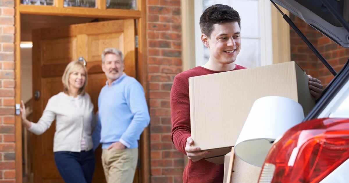 Young man packing a hatchback car with boxes & furniture with smiling parents in background