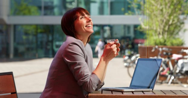 Professional woman seated in cafe with coffee and laptop smiling