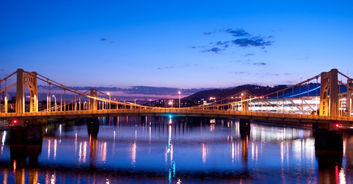 Two suspension bridges over a river in urban setting at dusk