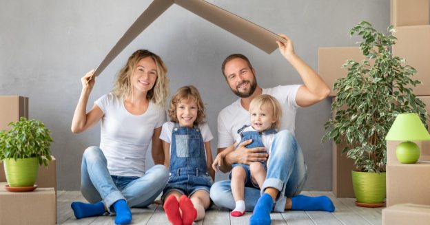 Mother and father with two young children seated on floor of room full of moving moxes