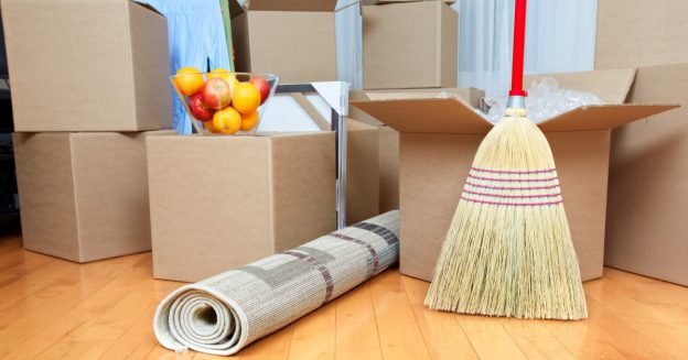 Broom, bowl of fruit, and rolled-up rug next to moving boxes