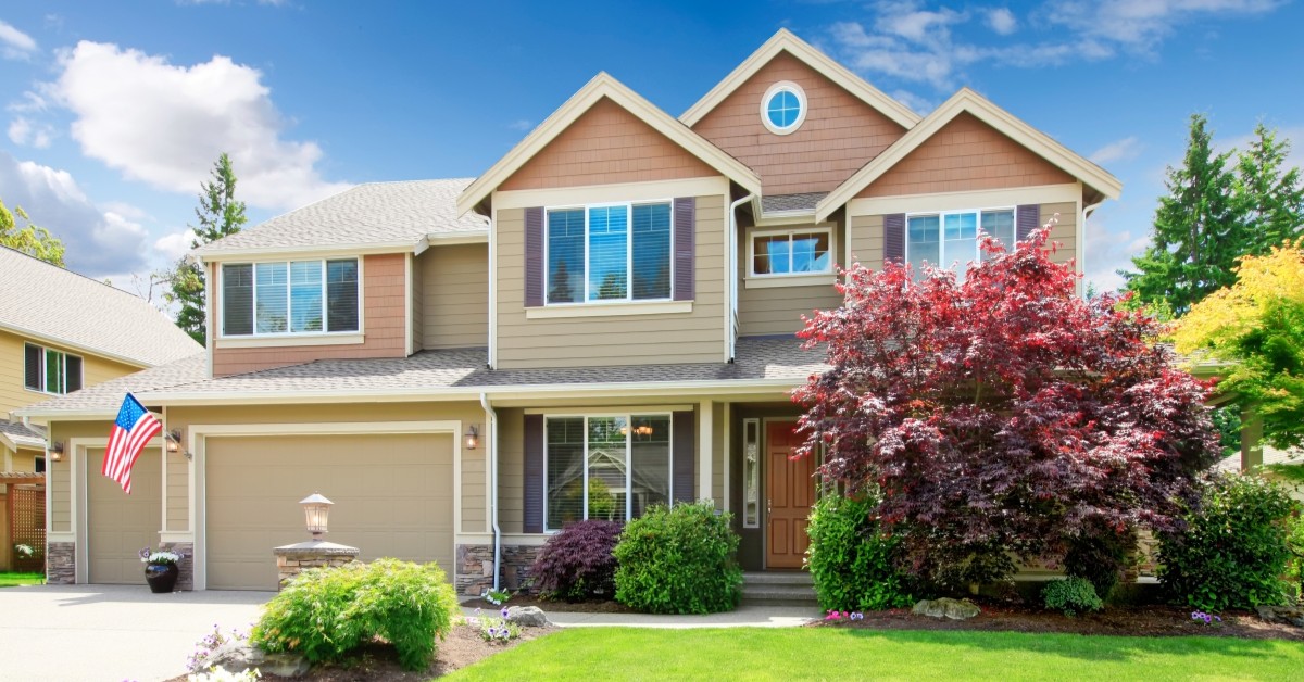 Light brown and beige two-story home with landscaping and American flag