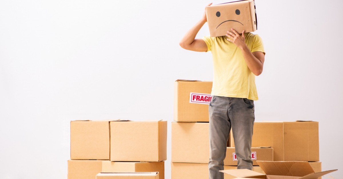 Man standing next to moving boxes and holding a box with a frown drawn on it