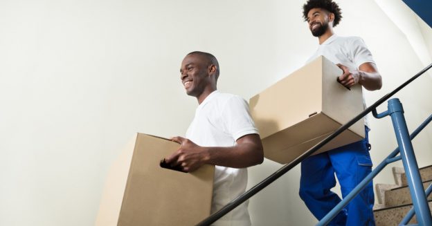 Two young men holding boxes and walking down a staircase