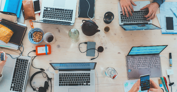 Work table with laptops, coffees, and electronics