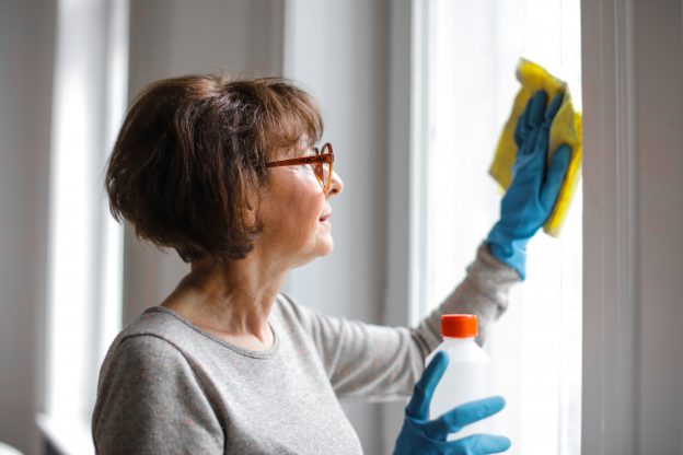 Woman with cleaning gloves and yellow towel cleaning window